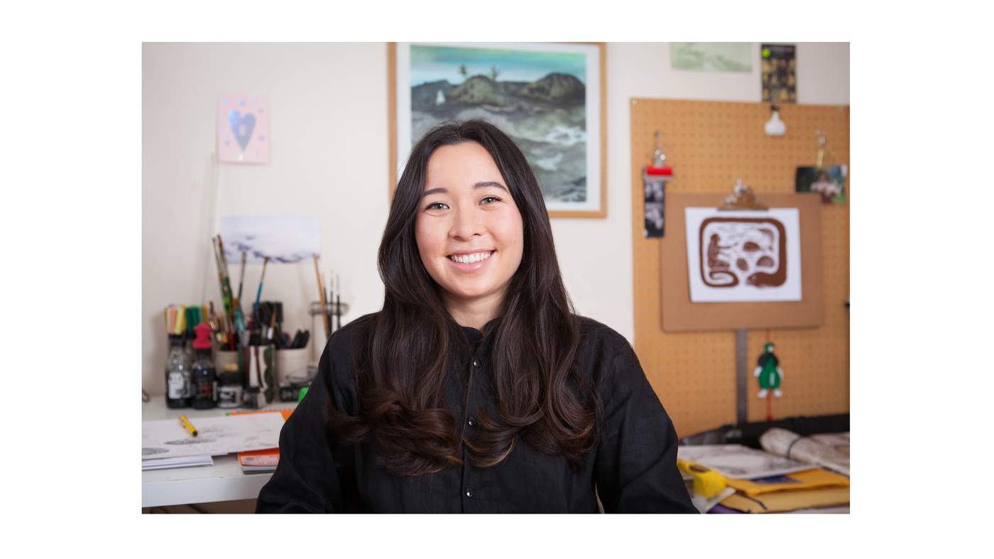 Photo of artist Emily Hughes in front of her desk and artwork.