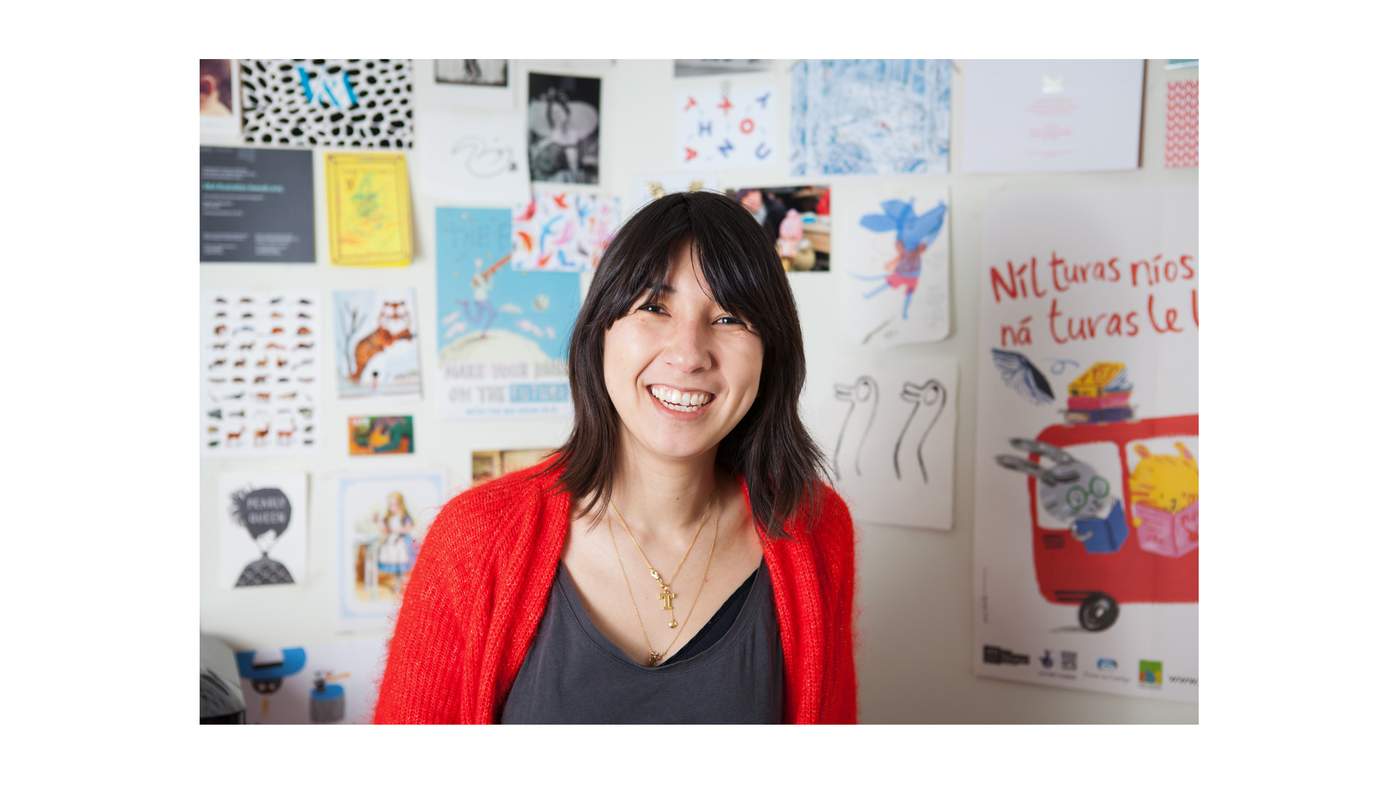 A photo of artist Yasmeen Ismail in front of a wall of her drawings.