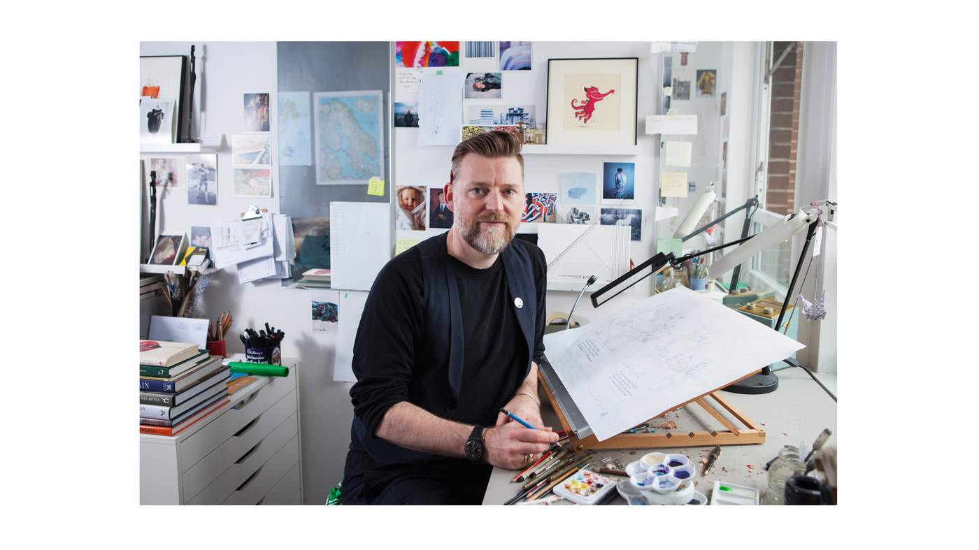 A photo of artist David Roberts at his desk by a window.