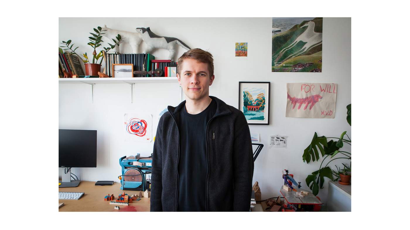 Photo of artist William Grill in front of his desk.